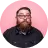 Reviewer photo of a bearded man with glasses on a pink background